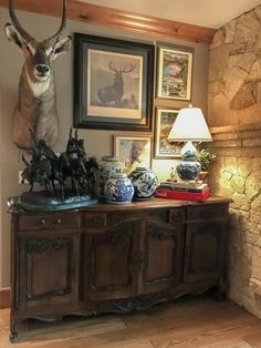 a deer head mounted on top of a wooden cabinet next to a lamp and pictures