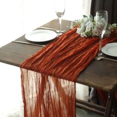 the table is set with plates, silverware and an orange scarf