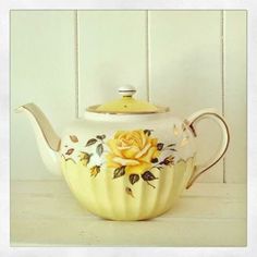 a tea pot with a yellow rose painted on the front and sides, sitting on a white surface