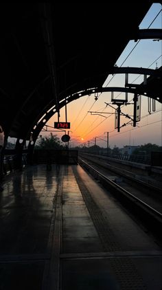 the sun is setting at an empty train station