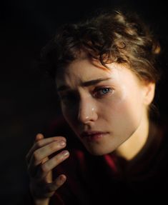 a close up of a person wearing a red shirt and holding their hand near her face