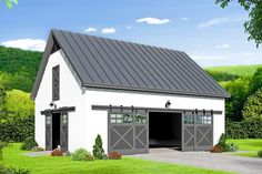 a large white barn with a black roof and two garage doors on the side of it