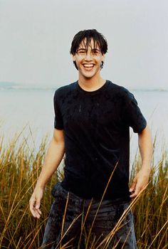 a man standing in tall grass next to the ocean