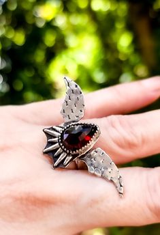 This unique garnet bat wing ring captures the essence of gothic elegance with its intricate design and striking appearance.   The centerpiece of the ring is a captivating garnet, known for its rich, deep red color and lustrous shine. Ring design size 1.8 inches wide × .9 inches long. Size 7. Ready to ship. Wing Ring, Gothic Elegance, Bat Wing, Deep Red Color, Statement Ring Silver, Intricate Design, Ring Sterling Silver, Bat Wings, Deep Red