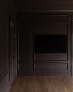 an empty room with wood floors and dark walls, has a flat screen tv on the wall