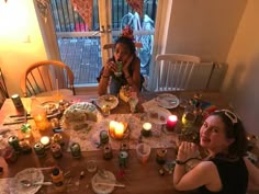 two women sitting at a table with candles in front of them and plates on the table