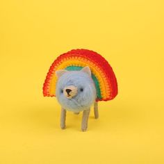 a stuffed animal with a rainbow colored hat on its head, standing in front of a yellow background