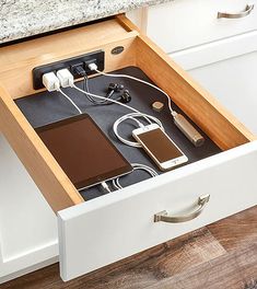 an open drawer in the middle of a kitchen counter with electronics inside and charging on it