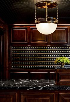 a chandelier hangs from the ceiling above a marble countertop in a dark wood paneled kitchen