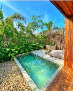 an outdoor swimming pool surrounded by greenery and wooden fenced in area with pillows on the side