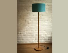 a wooden floor lamp with a blue shade on it's base and a cord plugged in