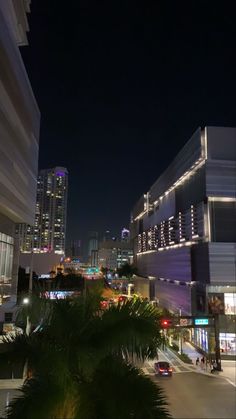 a city street at night with palm trees in the foreground and tall buildings on either side