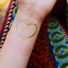 a woman's arm with a gold bracelet on it and a heart shaped charm