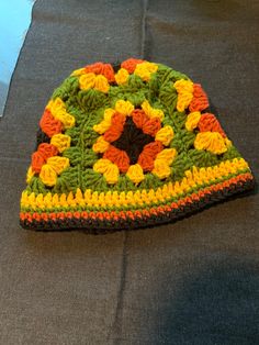 a crocheted sunflower hat sits on the ground next to a piece of fabric