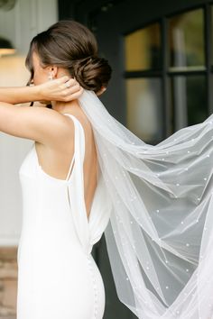 a woman in a white dress with a veil on her head and hands behind her back