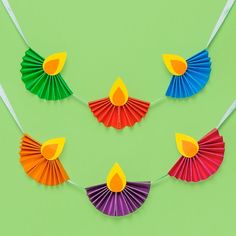 colorful paper fan decorations hanging from string on green background with white sticks and yellow candle