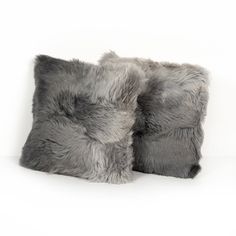 two gray pillows sitting next to each other on top of a white surface with one pillow covered in fur