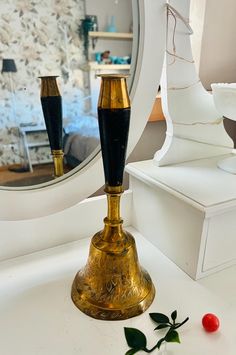 a gold and black vase sitting on top of a white counter next to a mirror