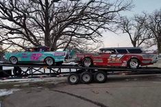 a flatbed tow truck carrying two classic cars on it's back in the snow