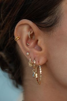 a woman wearing three different types of ear piercings on her left ear and the other one is gold