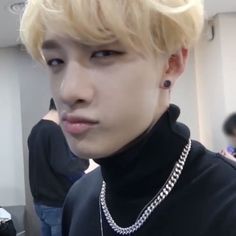 a young man with blonde hair wearing a black turtle neck sweater and silver chain necklace