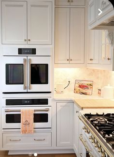 a kitchen with white cabinets and stainless steel stove top oven in the middle of it