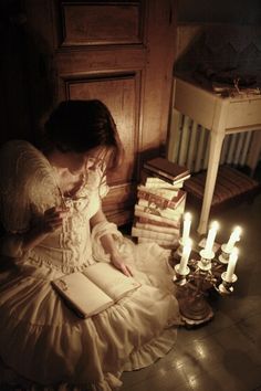 a woman sitting on the floor reading a book next to candles and bookshelves