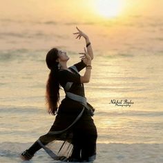 a woman standing on top of a beach next to the ocean with her arms in the air