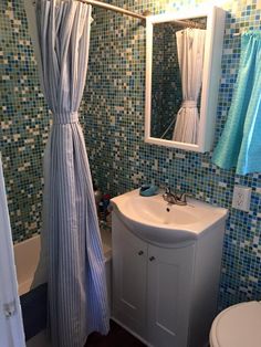 a bathroom with blue and white tile on the walls, shower curtain, sink and toilet