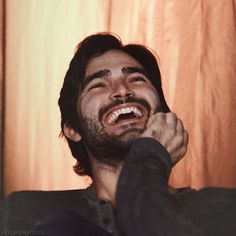 a man laughing while sitting in front of a curtain