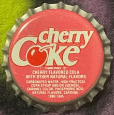 a close up of a bottle cap on a purple and green blanket with the word cherry coke in it