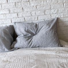 a bed with two pillows on top of it next to a white brick wall and floor