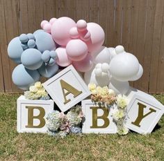 balloons and letters are arranged on the grass in front of a wooden fence with flowers