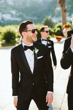 two men in tuxedos are walking down the street and one is taking a selfie