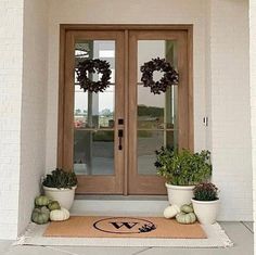 two potted plants are sitting on the front door mat, with wreaths and pumpkins