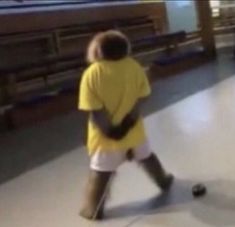 a boy in yellow shirt and white shorts playing with a soccer ball on the floor