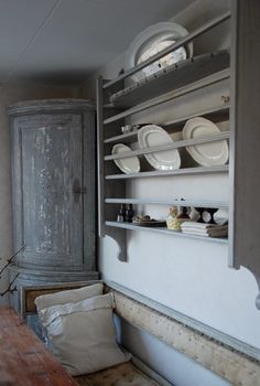 a wooden table topped with lots of white plates next to a wall mounted shelf filled with dishes