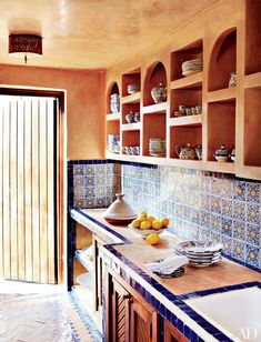 a kitchen with blue and white tiles on the counter tops, cabinets and shelves filled with dishes