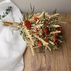 a bouquet of dried flowers sitting on top of a wooden table next to a white cloth