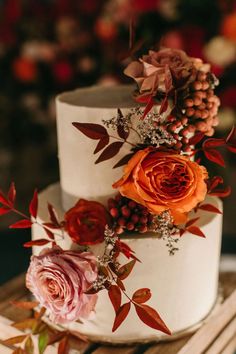 a three tiered cake with flowers and berries on the top is sitting on a wooden table