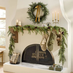 a fireplace with stockings and wreaths hanging on it's mantle next to candles