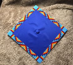 a blue square with an orange, yellow and red design on it sitting on a brown blanket