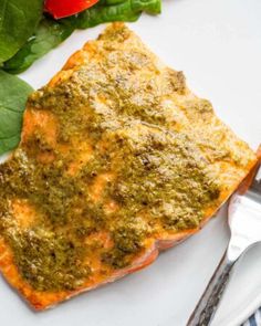 a piece of salmon covered in pesto on a white plate with a fork next to it