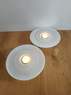 two white plates sitting on top of a wooden table next to a light bulb and cork