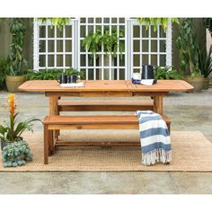 a wooden table with two benches and potted plants in front of it on a rug