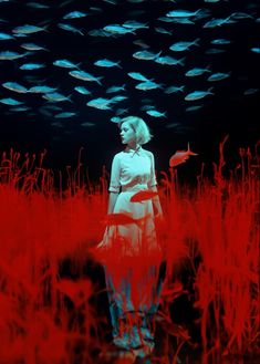 a woman is standing in the middle of a field with fish swimming around her and looking up into the sky