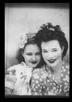 an old photo of two women with fake mouths and flowers on their heads, one woman is smiling at the camera