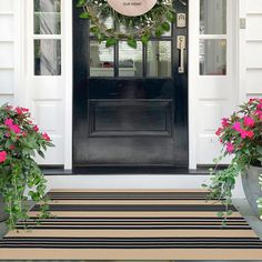 two potted flowers are on the front porch with a wreath and door mat in front of it