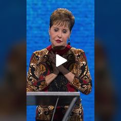 a woman standing at a podium in front of a blue screen with her hands folded