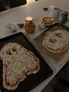 two uncooked pizzas sitting on top of baking pans covered in cheese